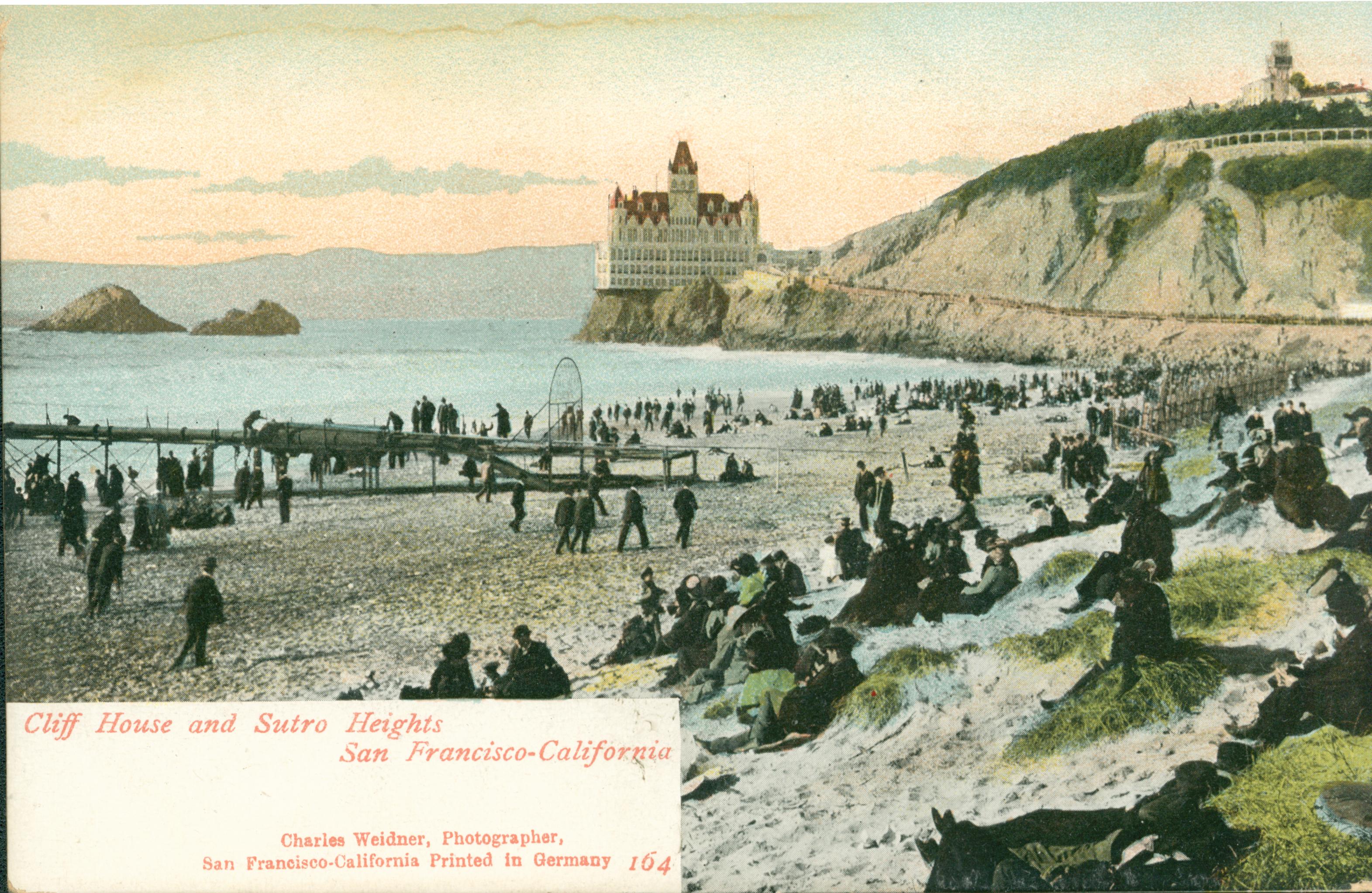 Shows the Cliff House, Seal Rocks and Sutro Heights, with individuals on the beach in the foreground.